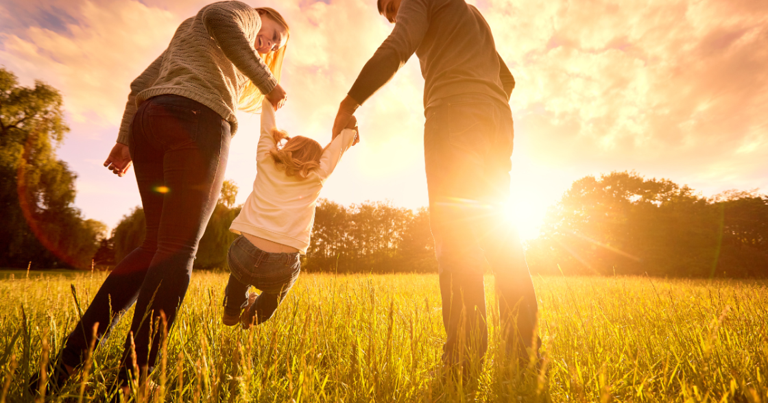 Two parents swinging their child in the air in a golden field